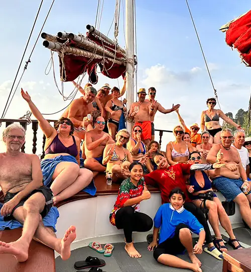 A large group of people pose for a group photo at sunset on a classic wooden boat booked for a private charter party. Krabi Private Party Boat