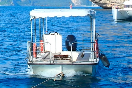 a small flat bottomed fibreglass boat with a full canopy and an outboard motor is being towed on clear calm water