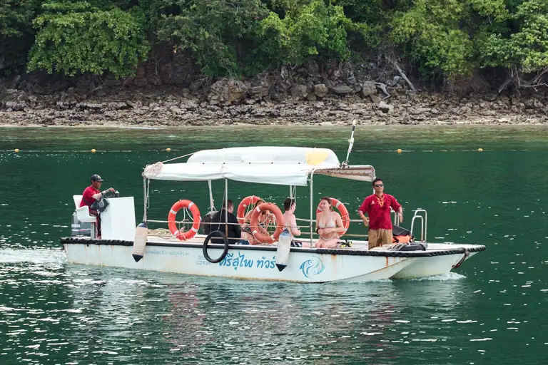 a flat bottom white, fibre glass boat with a full canopy and half a dozen people onboard, on a calm sea near Ao Nang Krabi