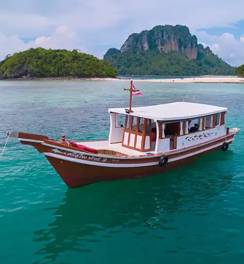A classic wooden boat moored at sea with beach tropical beach and island in the background